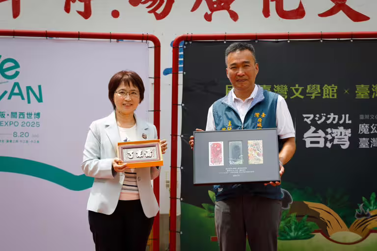 台文館陳瑩芳館長（左）手持府城隍廟郭榮哲主委致贈「爾來了」牌匾、郭榮哲（右）手持台文館回贈「魔幻台灣」特展書籤。   圖：台灣文學館提供